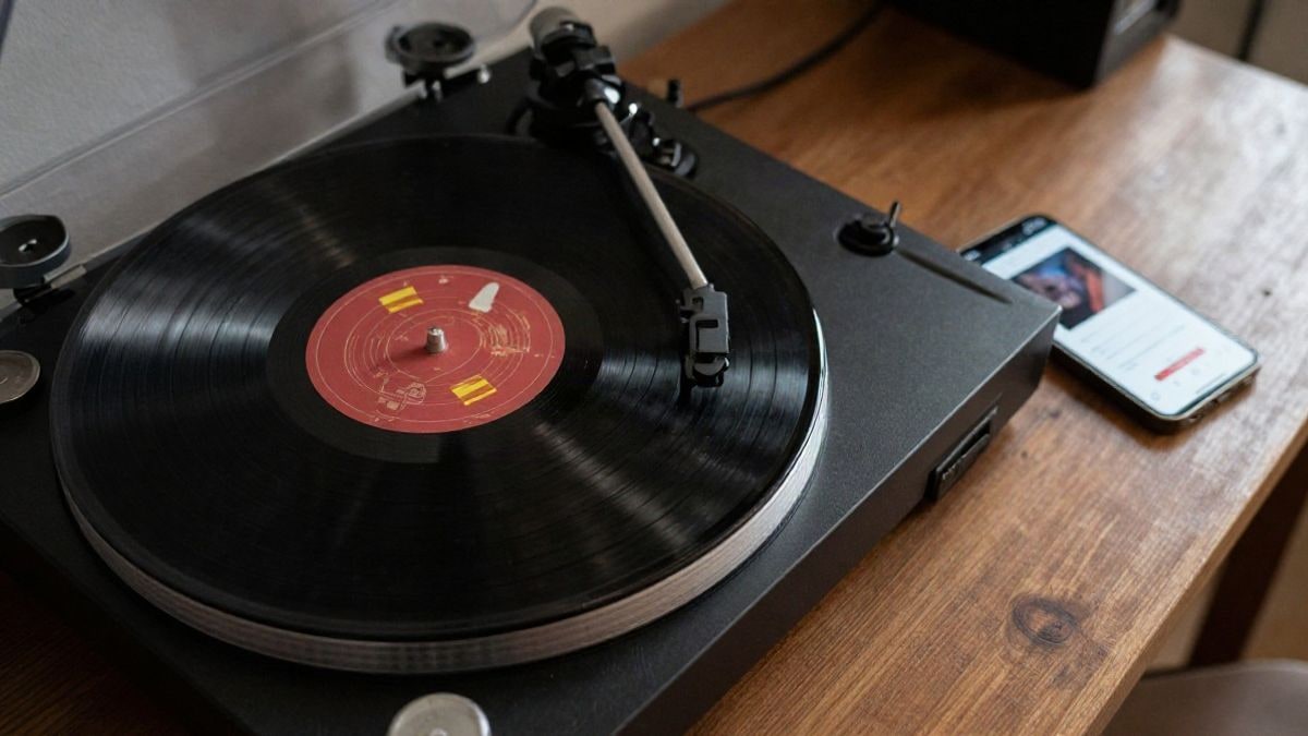 Imagen ilustrativa: vista cenital de un tocadiscos y un teléfono con una aplicación de música